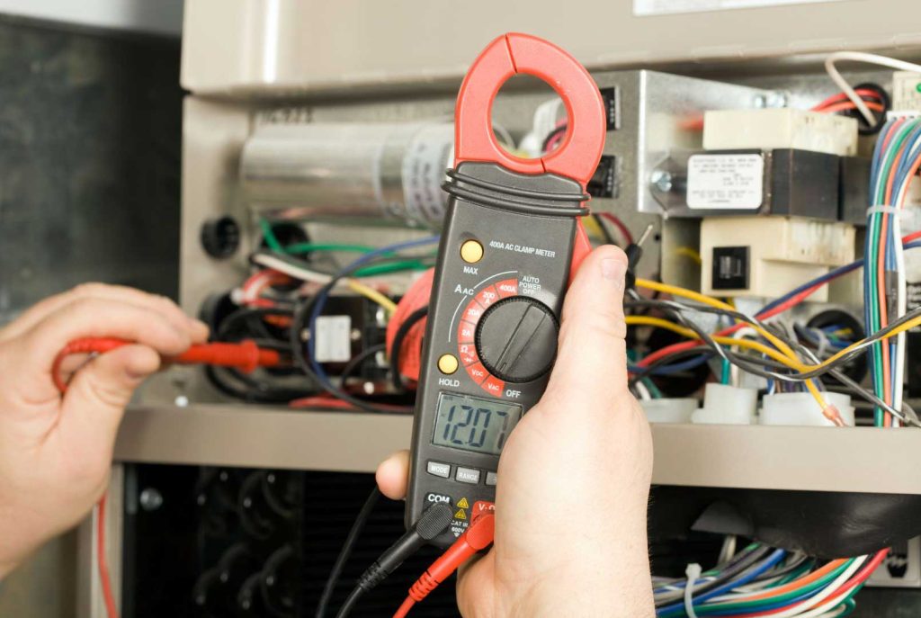 Technician using a clamp meter to test electrical components in an HVAC system