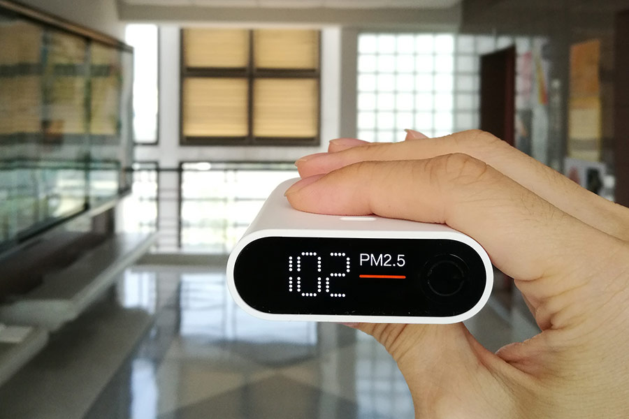 Hand holding a portable PM2.5 air quality monitor displaying 102